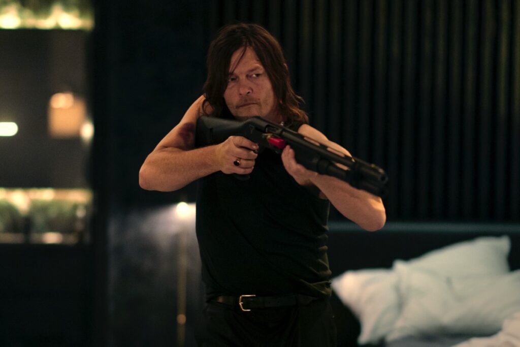 Man in shortsleeved black tee and jeans pointing a high-powered rifle